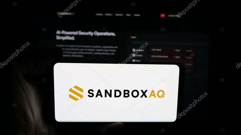 Stuttgart, Germany - 10-20-2025: Person holding cellphone with logo of US company SB Technology Inc. (SandboxAQ) on screen in front of webpage. Focus on phone display.
