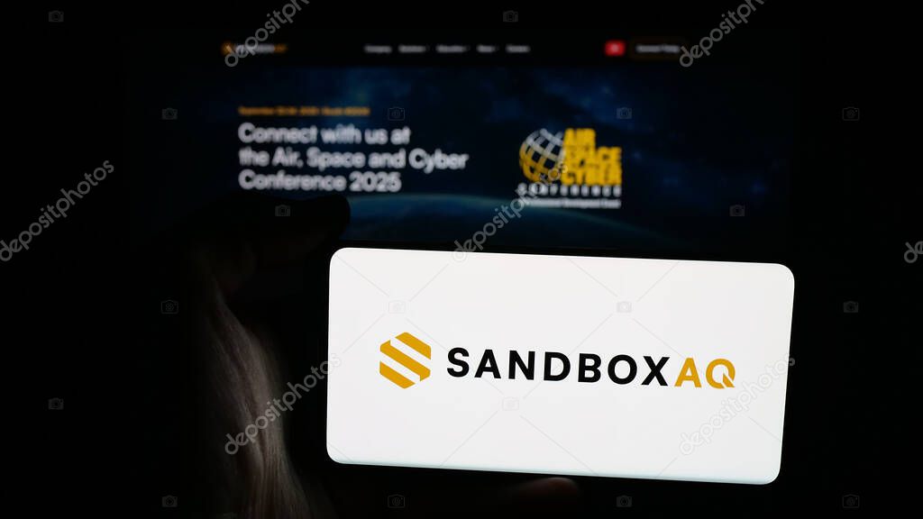 Stuttgart, Germany - 10-20-2025: Person holding mobile phone with logo of US company SB Technology Inc. (SandboxAQ) on screen in front of web page. Focus on phone display.