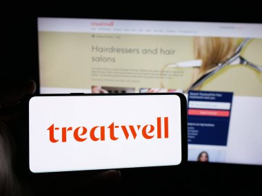 Stuttgart, Almanya - 10-25-2025: İnternet sitesinin önünde sağlık platformu şirketi Treatwell 'in logosuna sahip akıllı telefon sahibi kişi. Telefon ekranına odaklan.