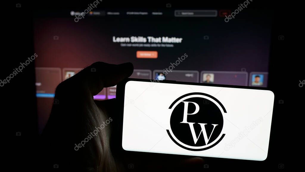 Stuttgart, Germany - 10-25-2025: Person holding mobile phone with logo of Indian company Physics Wallah Limited (PW) on screen in front of web page. Focus on phone display.