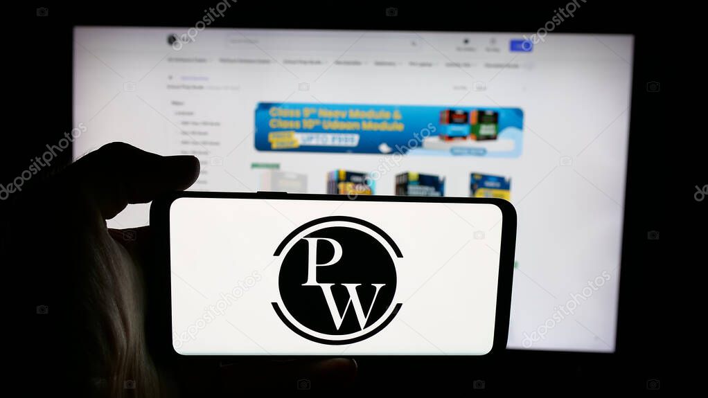Stuttgart, Germany - 10-25-2025: Person holding cellphone with logo of Indian company Physics Wallah Limited (PW) on screen in front of webpage. Focus on phone display.