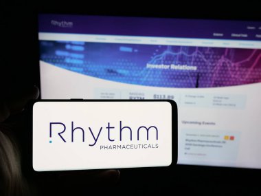 Stuttgart, Almanya - 10-30-2025: Sitenin önünde ekranda biyofarma şirketi Rhythm Pharmaceuticals Inc. 'in logosuna sahip akıllı telefonu tutan kişi. Telefon ekranına odaklan.