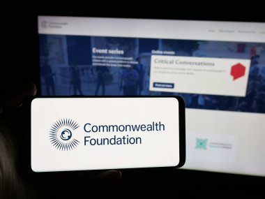Stuttgart, Almanya - 10-30-2025: Sitenin önünde ekranda Commonwealth Foundation organizasyonu logosu olan akıllı telefon sahibi kişi. Telefon ekranına odaklan.