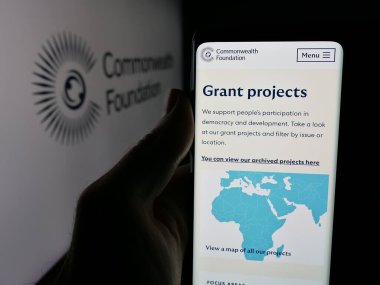 Stuttgart, Almanya - 10-30-2025: Commonwealth Foundation organizasyonunun web sayfası olan akıllı telefonu logo önünde ekranda tutan kişi. Telefon ekranının merkezine odaklan.