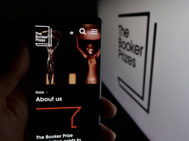 Stuttgart, Almanya - 10-30-2025: İngiliz Edebiyat Ödülü Booker Ödülü web sayfası logosu önünde cep telefonu tutan kişi. Telefon ekranının merkezine odaklan.