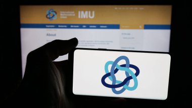 Stuttgart, Almanya - 10-31-2025: İnternet sayfası önünde Uluslararası Matematik Birliği (IMU) logosu olan cep telefonu sahibi kişi. Telefon ekranına odaklan.