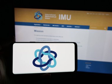 Stuttgart, Almanya - 10-31-2025: İnternet sitesi önünde üzerinde Uluslararası Matematik Birliği (IMU) logosu bulunan akıllı telefon sahibi kişi. Telefon ekranına odaklan.