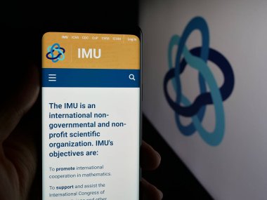 Stuttgart, Almanya - 10-31-2025: Logo önündeki ekranda Uluslararası Matematik Birliği (IMU) web sayfası bulunan kişi. Telefon ekranının merkezine odaklan.