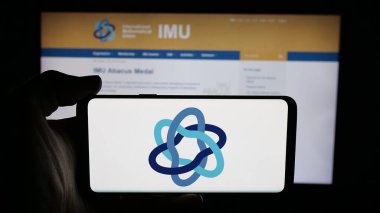 Stuttgart, Almanya - 10-31-2025: İnternet sayfası önünde Uluslararası Matematik Birliği (IMU) logosu olan cep telefonu sahibi kişi. Telefon ekranına odaklan.