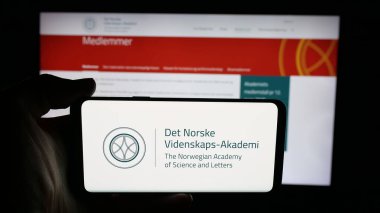 Stuttgart, Almanya - 10-31-2025: İnternet sayfası önünde Norveç Bilim ve Edebiyat Akademisi logosu bulunan kişi. Telefon ekranına odaklan.