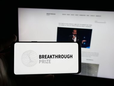 Stuttgart, Almanya - 10-31-2025: İnternet sitesi önünde elinde uluslararası ödül amblemli akıllı telefon bulunduran kişi. Telefon ekranına odaklan.