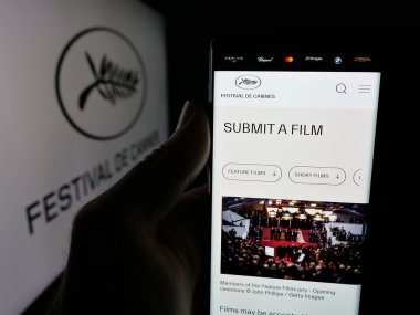 Stuttgart, Almanya - 10-31-2025: Uluslararası etkinlik Cannes Film Festivali web sitesi ile akıllı telefonu logonun önünde ekranda tutan kişi. Telefon ekranının merkezine odaklan.