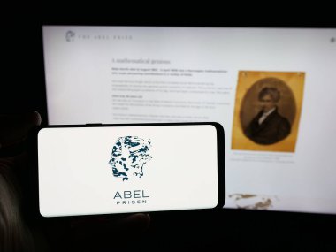 Stuttgart, Almanya - 10-31-2025: Web sitesi önünde üzerinde matematik ödülü logosu olan akıllı telefon sahibi kişi. Telefon ekranına odaklan.