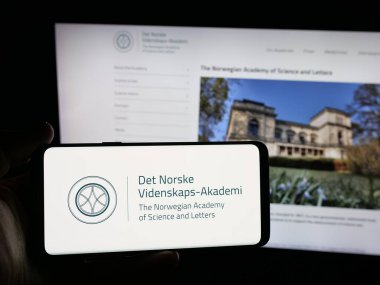 Stuttgart, Almanya - 10-31-2025: İnternet sitesi önünde Norveç Bilim ve Edebiyat Akademisi logosu bulunan kişi. Telefon ekranına odaklan.