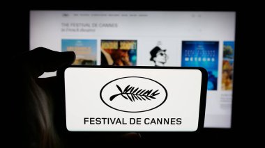 Stuttgart, Almanya - 10-31-2025: Cannes Film Festivali uluslararası etkinlik logosu ile cep telefonunu web sayfası önünde tutan kişi. Telefon ekranına odaklan.