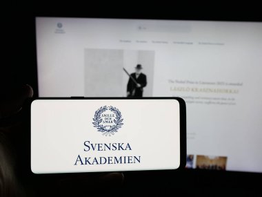 Stuttgart, Almanya - 10-31-2025: İnternet sitesi önünde Svenska Akademien 'in (İsveç Akademisi) logosunu taşıyan kişi. Telefon ekranına odaklan.