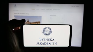 Stuttgart, Almanya - 10-31-2025: Web sayfası önünde Svenska Akademien (İsveç Akademisi) logosunun bulunduğu cep telefonu sahibi kişi. Telefon ekranına odaklan.