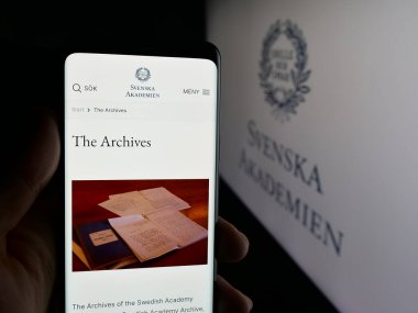 Stuttgart, Almanya - 10-31-2025: Logo önündeki ekranda Svenska Akademien 'in (İsveç Akademisi) web sayfası bulunan kişi. Telefon ekranının merkezine odaklan.
