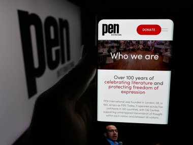 Stuttgart, Almanya - 10-31-2025: Yazarlar Birliği PEN International 'ın web sayfası olan akıllı telefonu logonun önünde ekranda tutan kişi. Telefon ekranının merkezine odaklan.