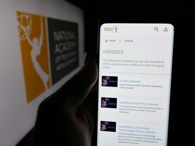 Stuttgart, Almanya - 10-31-2025: ABD televizyon ödülü Emmy Ödülleri (Emmy Ödülleri) web sayfası logonun önünde duran kişi. Telefon ekranının merkezine odaklan.