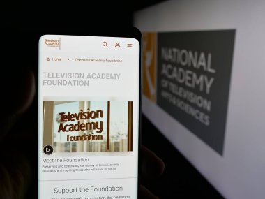 Stuttgart, Almanya - 10-31-2025: ABD televizyon ödülü Emmy Ödülleri (Emmy Ödülleri) web sayfası logonun önünde cep telefonu tutan kişi. Telefon ekranının merkezine odaklan.