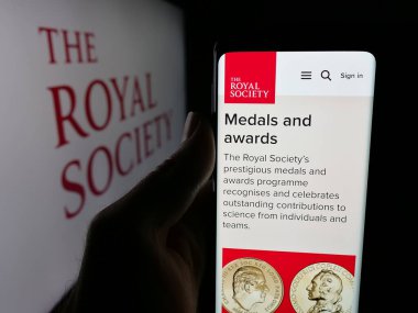 Stuttgart, Almanya - 11-01-2025: İngiliz Kraliyet Topluluğu 'nun logo önündeki web sayfası ile cep telefonu tutan kişi. Telefon ekranının merkezine odaklan.