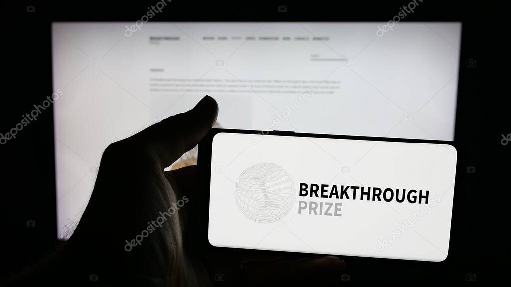 Stuttgart, Germany - 10-31-2025: Person holding mobile phone with logo of international awards Breakthrough Prizes on screen in front of web page. Focus on phone display.
