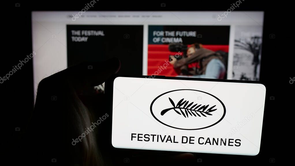 Stuttgart, Germany - 10-31-2025: Person holding mobile phone with logo of international event Cannes Film Festival on screen in front of web page. Focus on phone display.