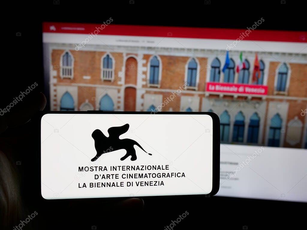 Stuttgart, Germany - 10-31-2025: Person holding smartphone with logo of Venice Film Festival (Biennale) on screen in front of website. Focus on phone display.