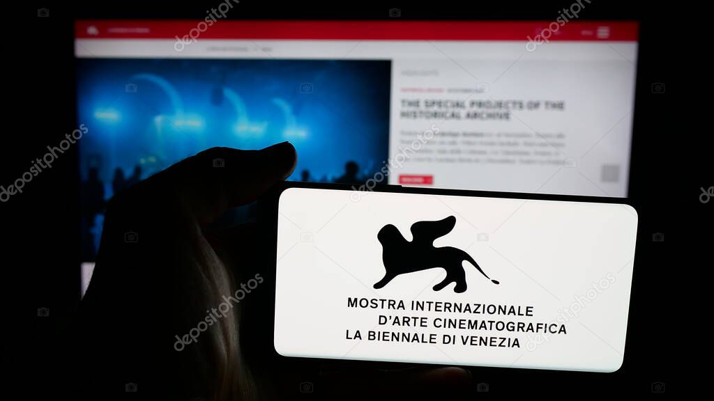 Stuttgart, Germany - 10-31-2025: Person holding mobile phone with logo of Venice Film Festival (Biennale) on screen in front of web page. Focus on phone display.