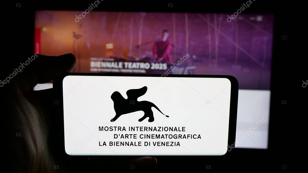 Stuttgart, Germany - 10-31-2025: Person holding cellphone with logo of Venice Film Festival (Biennale) on screen in front of webpage. Focus on phone display.