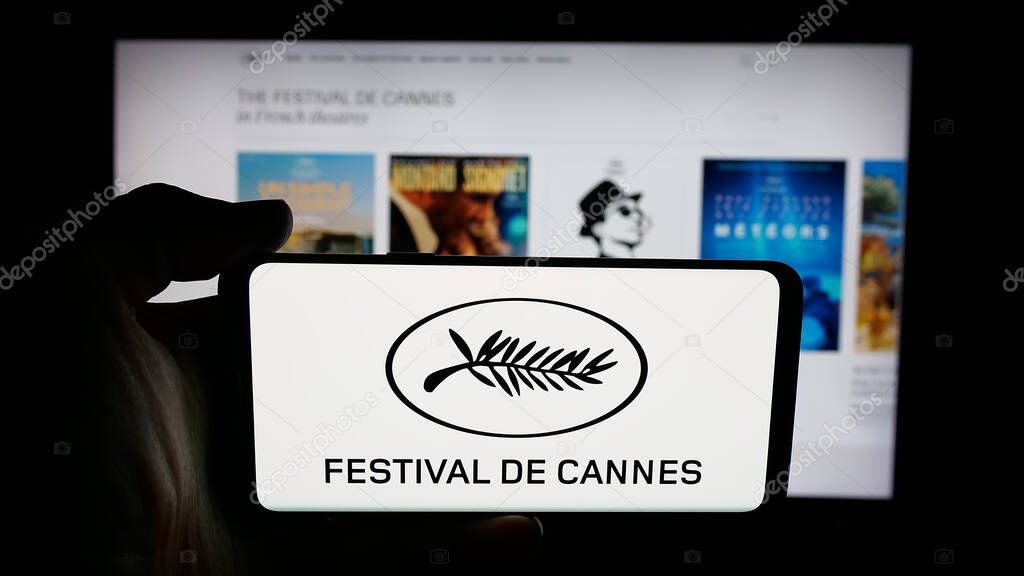 Stuttgart, Germany - 10-31-2025: Person holding cellphone with logo of international event Cannes Film Festival on screen in front of webpage. Focus on phone display.