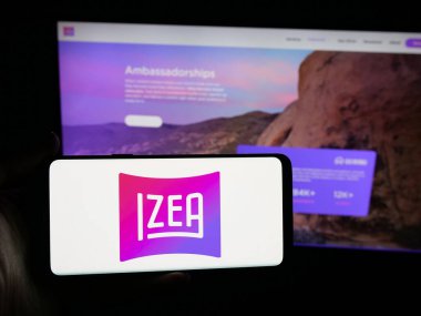 Stuttgart, Almanya - 11-02-2025: İnternet sitesi önünde üzerinde IZEA Worldwide Inc. 'in logosu bulunan akıllı telefon sahibi kişi. Telefon ekranına odaklan.