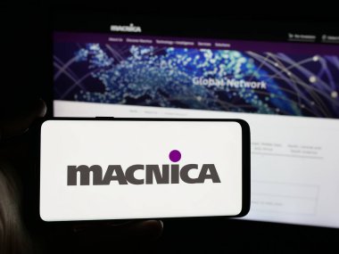 Stuttgart, Almanya - 11-02-2025: Japon teknoloji şirketi Macnica Inc. 'in logosunu elinde tutan kişi web sitesinin önünde ekranda. Telefon ekranına odaklan.