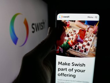 Stuttgart, Germany - 11-03-2025: Person holding smartphone with web page of Swedish fintech company Swish (Getswish AB) on screen in front of logo. Focus on center of phone display.