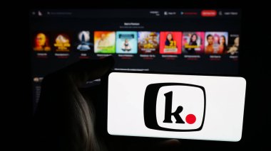 Stuttgart, Germany - 11-03-2025: Person holding mobile phone with logo of Indian platform company Kuku FM (kukufm.com) on screen in front of web page. Focus on phone display.