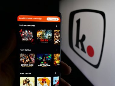 Stuttgart, Germany - 11-03-2025: Person holding smartphone with web page of Indian platform company Kuku FM (kukufm.com) on screen in front of logo. Focus on center of phone display.