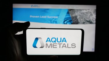 Stuttgart, Germany - 11-04-2025: Person holding cellphone with logo of US metal recycling company Aqua Metals Inc. on screen in front of webpage. Focus on phone display.