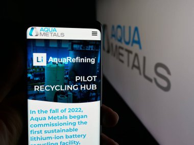 Stuttgart, Germany - 11-04-2025: Person holding smartphone with web page of US metal recycling company Aqua Metals Inc. on screen in front of logo. Focus on center of phone display.