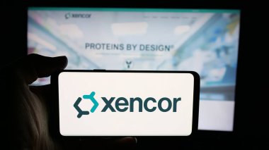 Stuttgart, Germany - 11-04-2025: Person holding cellphone with logo of US biotechnology company Xencor Inc. on screen in front of webpage. Focus on phone display.