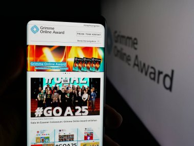 Stuttgart, Germany - 11-05-2025: Person holding cellphone with webpage of German media prize Grimme Online Award on screen in front of logo. Focus on center of phone display.