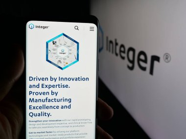 Stuttgart, Germany - 11-05-2025: Person holding cellphone with webpage of US company Integer Holdings Corporation on screen in front of logo. Focus on center of phone display.