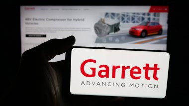Stuttgart, Germany - 11-05-2025: Person holding mobile phone with logo of US automotive company Garrett Motion Inc. on screen in front of web page. Focus on phone display.