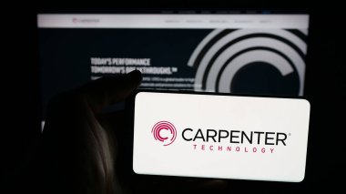 Stuttgart, Germany - 11-05-2025: Person holding mobile phone with logo of US company Carpenter Technology Corporation on screen in front of web page. Focus on phone display.