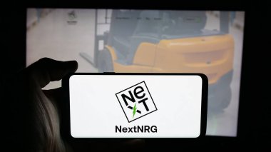 Stuttgart, Germany - 11-06-2025: Person holding cellphone with logo of US fuel distribution company NextNRG Inc. on screen in front of webpage. Focus on phone display.