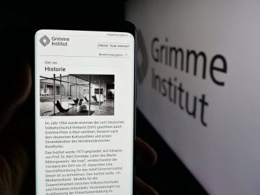 Stuttgart, Germany - 11-06-2025: Person holding cellphone with webpage of German media organisation Grimme-Institut on screen in front of logo. Focus on center of phone display.