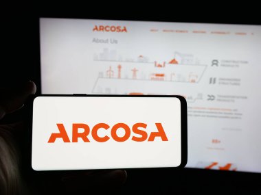 Stuttgart, Germany - 11-07-2025: Person holding smartphone with logo of US infrastructure company Arcosa Inc. on screen in front of website. Focus on phone display.