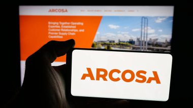 Stuttgart, Germany - 11-07-2025: Person holding mobile phone with logo of US infrastructure company Arcosa Inc. on screen in front of web page. Focus on phone display.