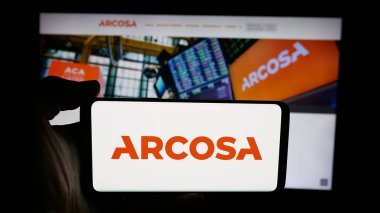 Stuttgart, Germany - 11-07-2025: Person holding cellphone with logo of US infrastructure company Arcosa Inc. on screen in front of webpage. Focus on phone display.