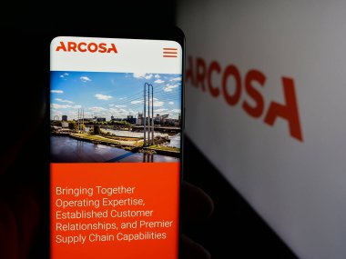 Stuttgart, Germany - 11-07-2025: Person holding cellphone with webpage of US infrastructure company Arcosa Inc. on screen in front of logo. Focus on center of phone display.